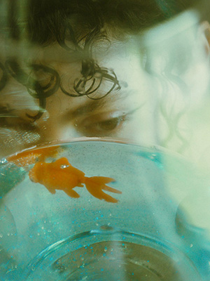 Model looks at a goldfish through glass with the goldfish floating around