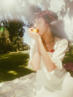 Model gently bite a lemon as she sits down on her picnic sheet looking at the lemon