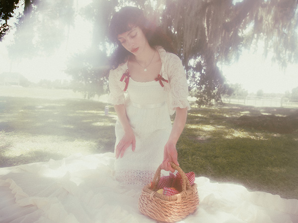 Model sitting on her picnic sheet as she gently picks up a fruit picnic basket while looking at it