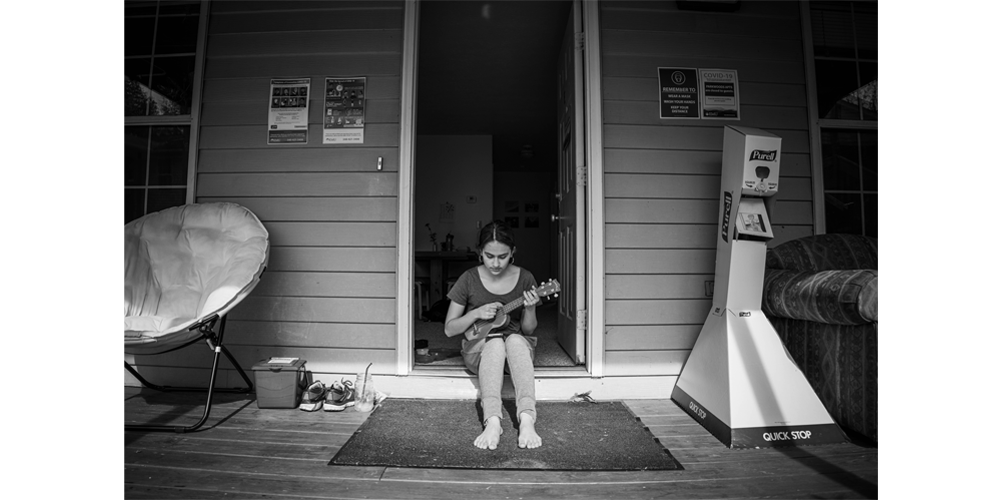 Hannah sits in her apartment doorframe playing ukulele and singing in the sun.