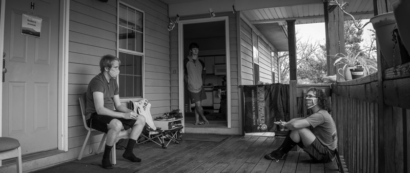 Black and white image of three friends sitting on a porch.