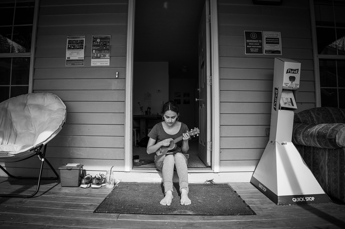 Hannah sits in her apartment doorframe playing ukulele and singing in the sun.